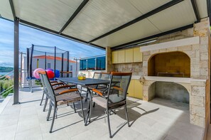 An outdoor patio with a table and chairs, a brick oven, and a view of the sea. - Villa Urban (Okrug Gornji)