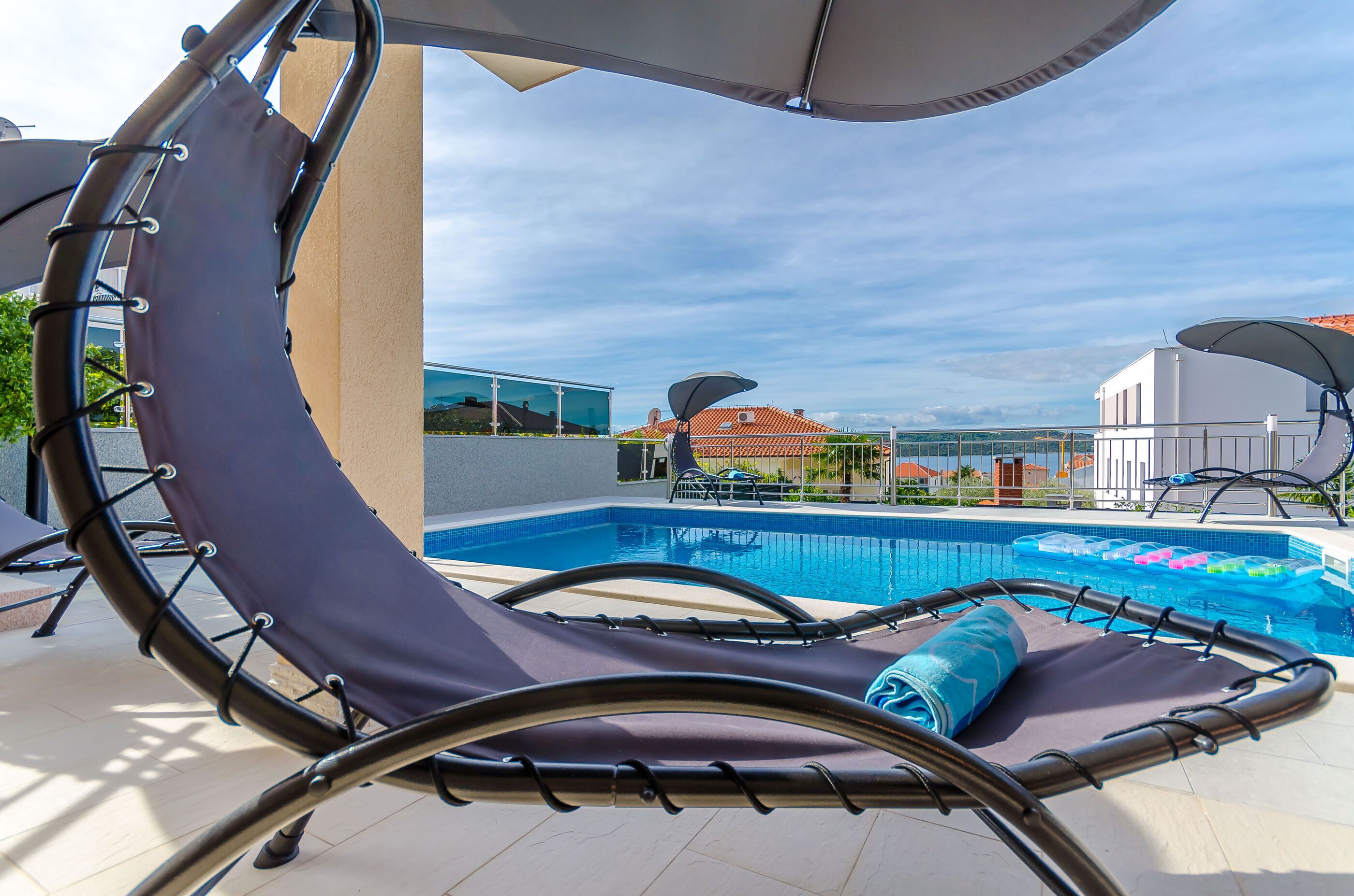 A poolside lounge chair with a towel, a pool, and a view of buildings in the background.