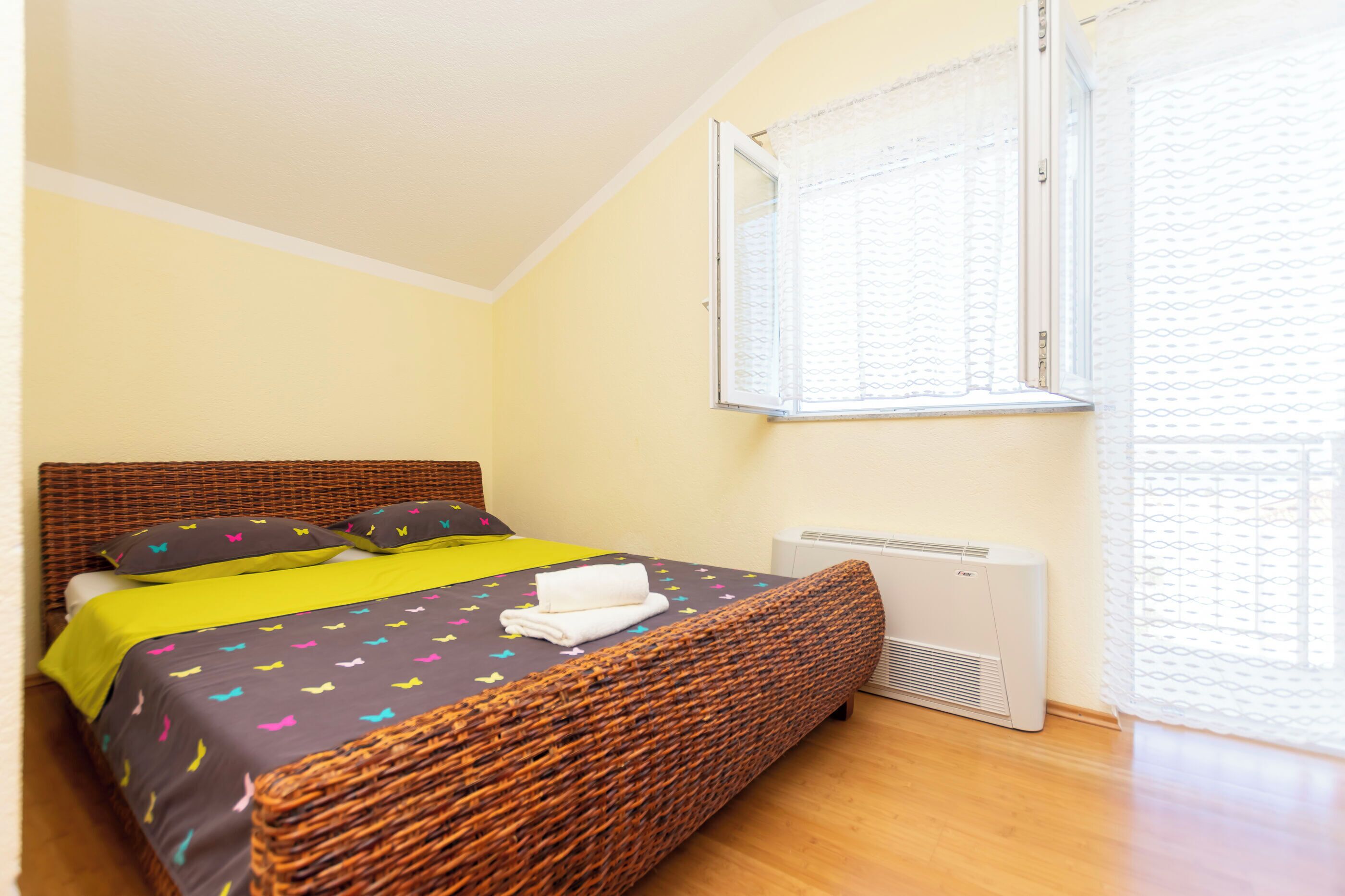 Un lit avec une tête de lit en osier, une couvre-lit jaune et des coussins colorés.