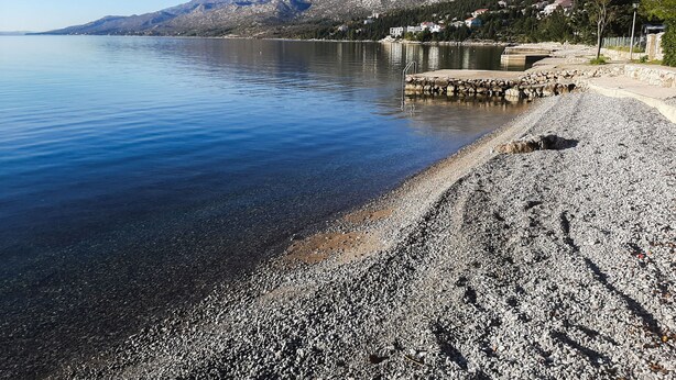 A pebble beach with a stone jetty and houses in the background. - Apartment Anica (Starigrad - Paklenica)