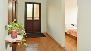 A hallway with a wooden door, a small table with a potted plant, and a bed in the adjacent room. - Apartment Anica (Starigrad - Paklenica)
