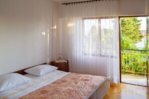 A bedroom with a bed, a nightstand, and a view of a balcony with greenery. - Apartment Anica (Starigrad - Paklenica)