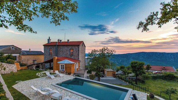 Une maison en pierre avec une piscine, des chaises longues et une vue sur les montagnes.