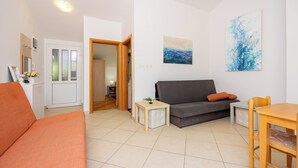 A living room with a sofa, a dining table, and a small side table with a plant. - Apartments Petak (Dramalj)