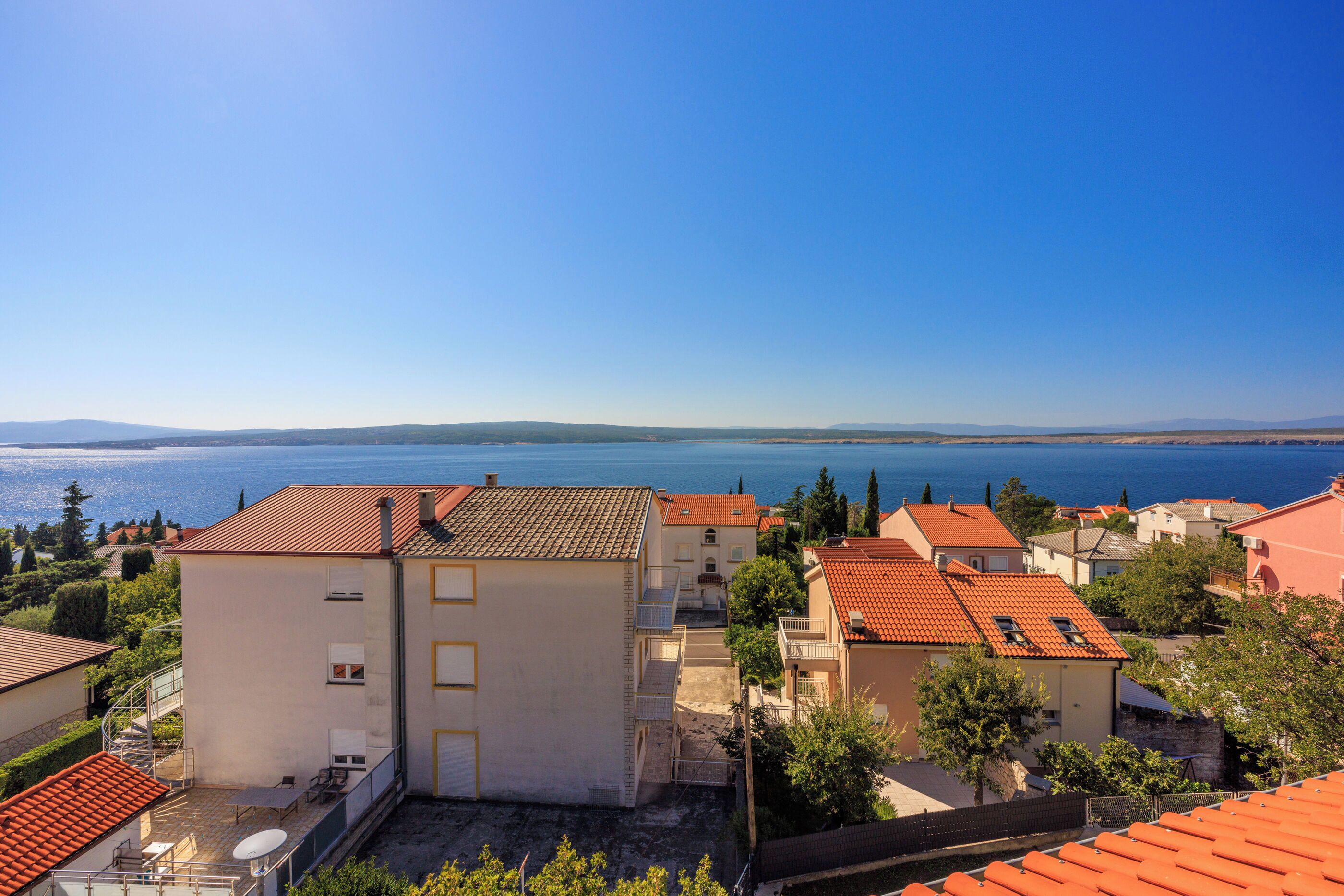 A coastal residential area with buildings featuring red-tiled roofs and balconies overlooking the sea.