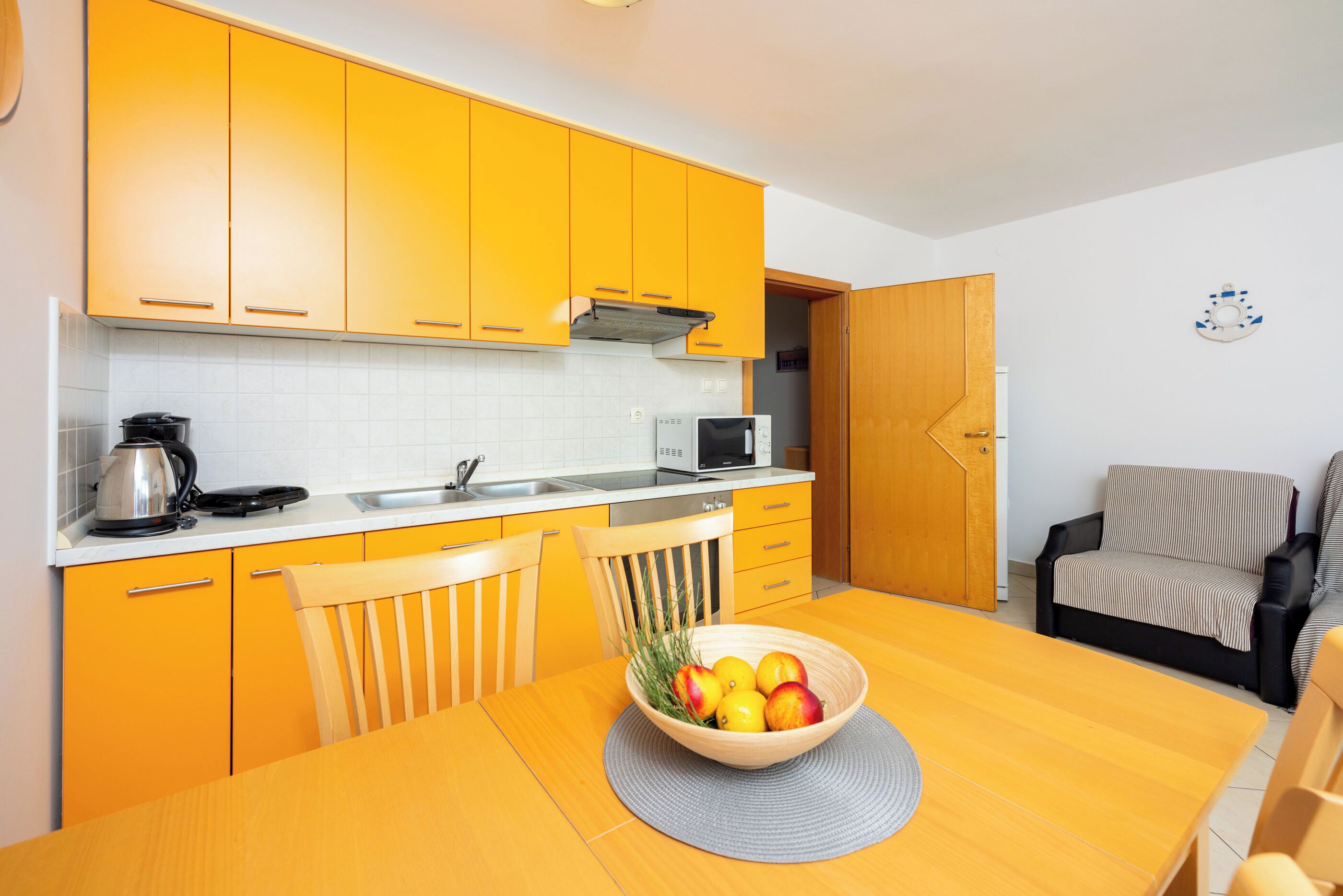 A compact kitchen with yellow cabinets, a microwave, and a kettle on the counter.