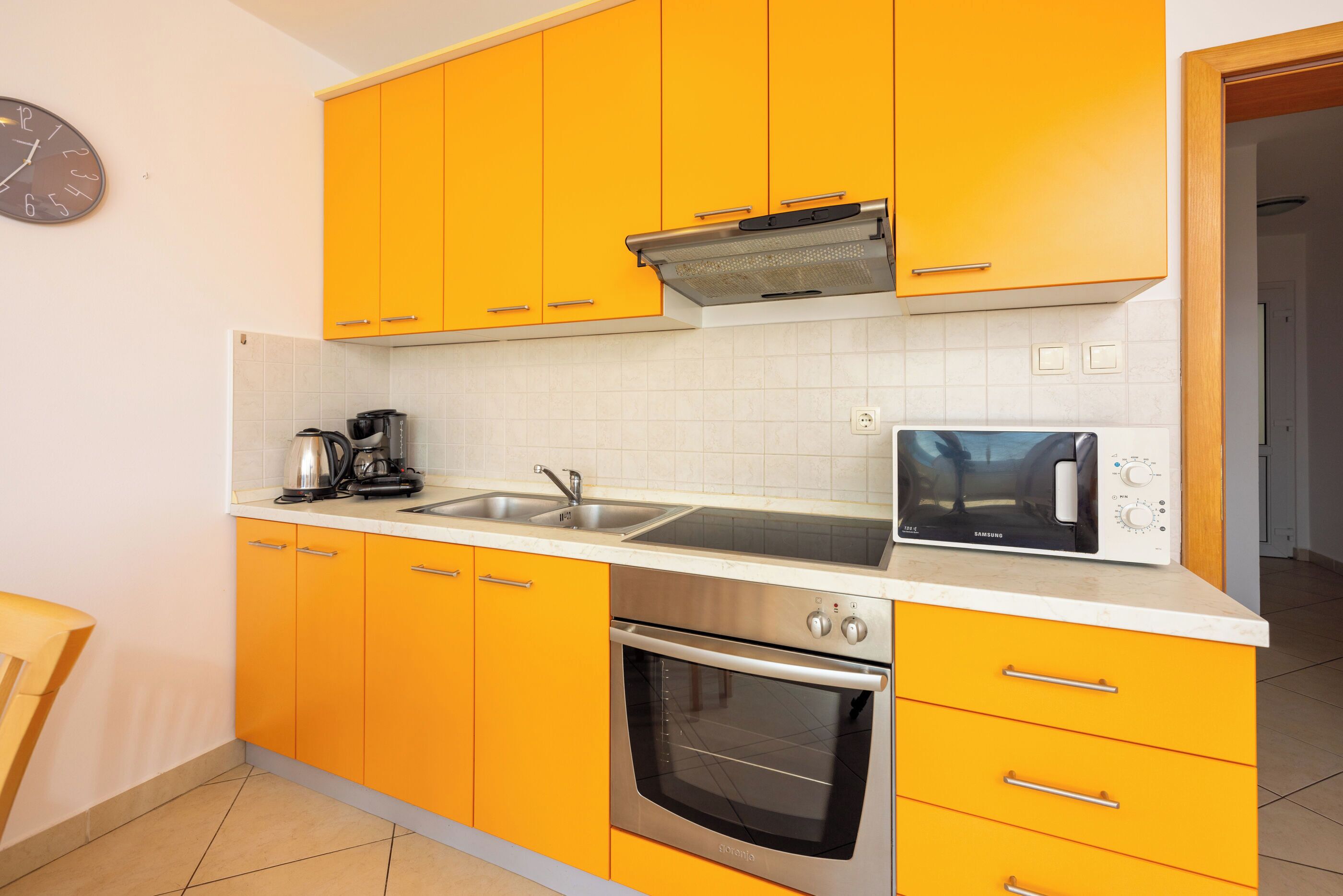 A kitchen with yellow cabinets, a stainless steel oven, a microwave, and a coffee maker.