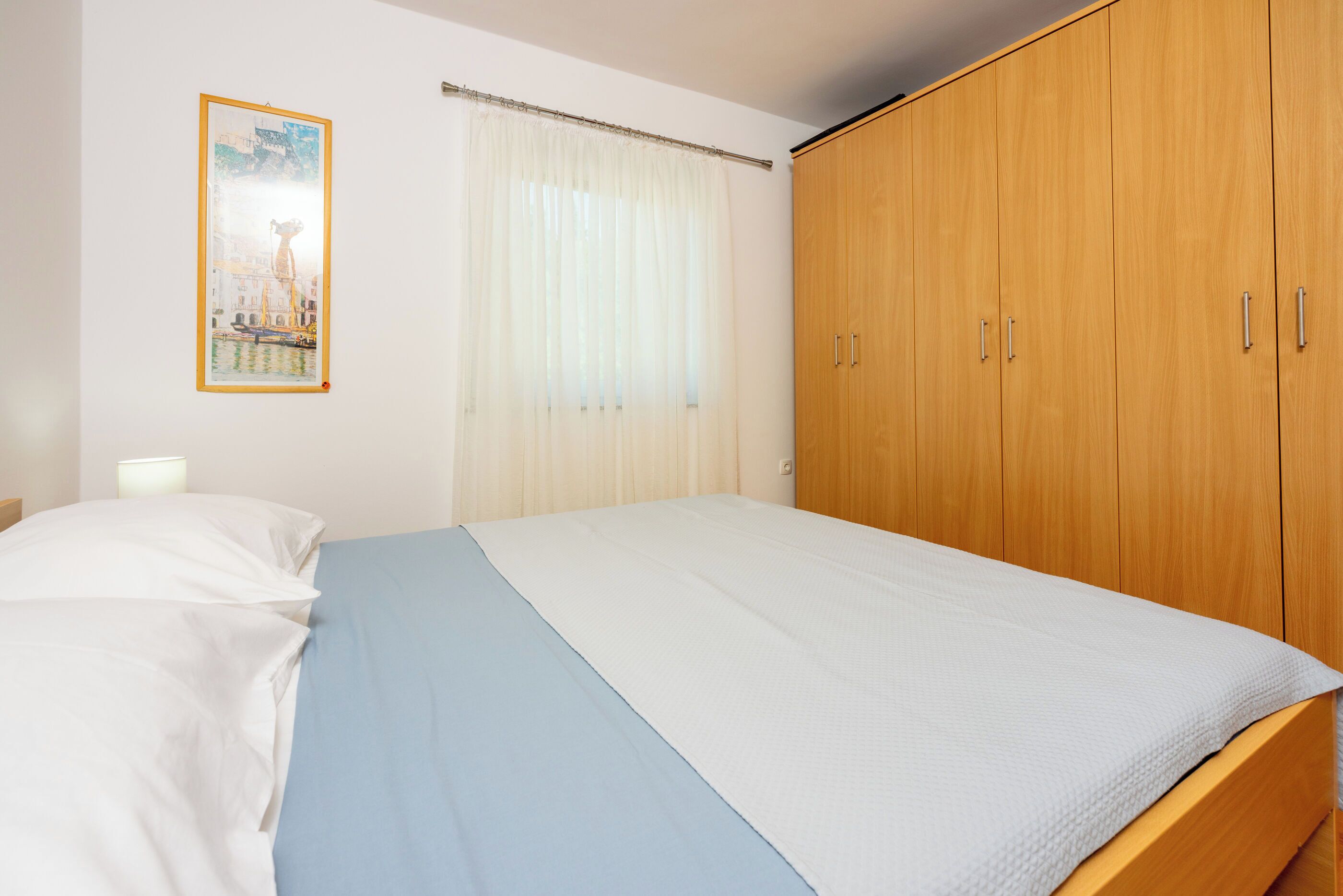 Une chambre à coucher avec un lit, une armoire en bois, un rideau et un tableau encadré accroché au mur.