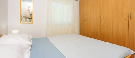 Une chambre à coucher avec un lit, une armoire en bois, un rideau et un tableau encadré accroché au mur.