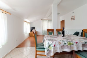 A dining area with a table set for two, a television in the background, and a view of the living room. - Apartments Slavica (Lopar)