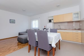 A dining area with a table, chairs, a sofa, and a kitchen with cabinets and a microwave. - Apartments Slavica (Lopar)