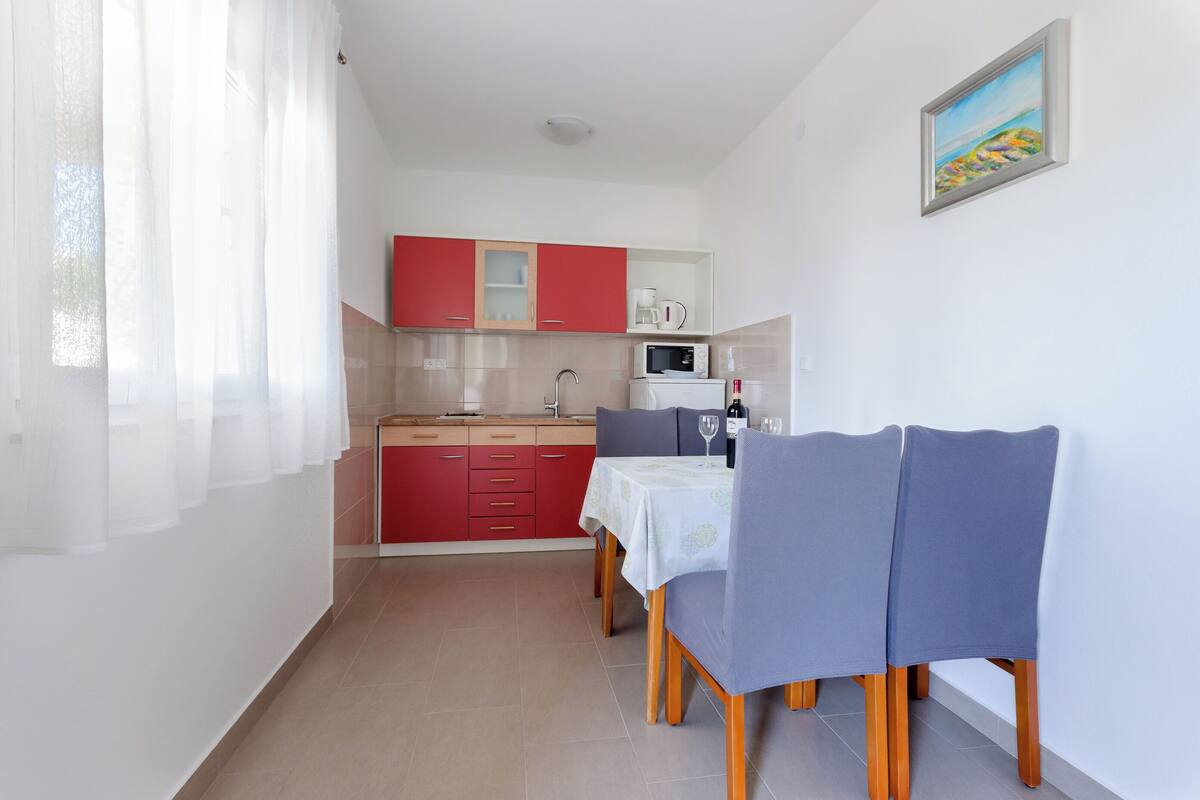 A compact kitchen with red cabinets, a microwave, and a dining area with a table and chairs.