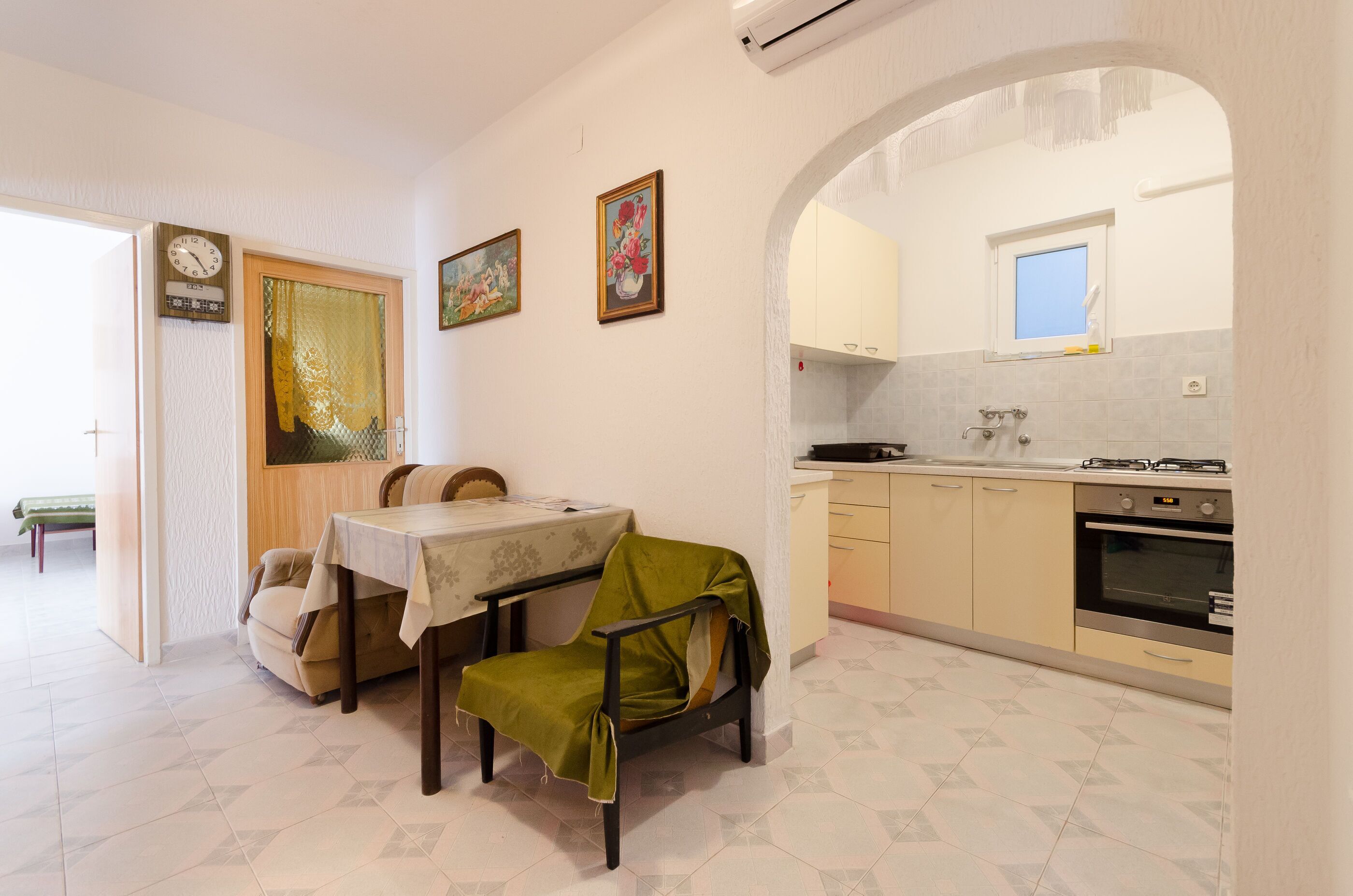 A dining area with a table and chairs, a kitchen with cabinets and an oven, and a clock on the wall.