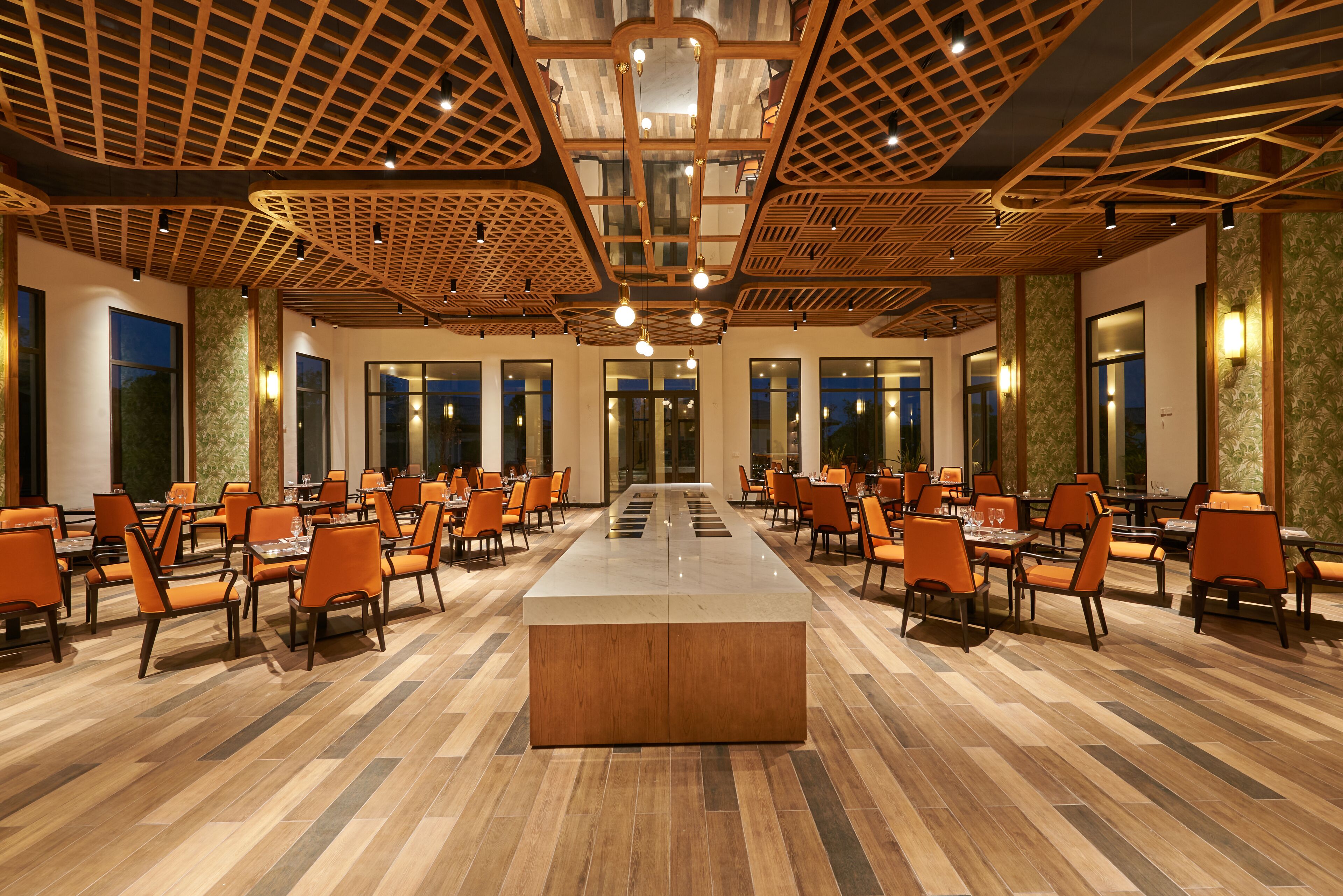 A spacious conference room with a central table, surrounded by rows of orange chairs, and a wooden ceiling with a geometric design.