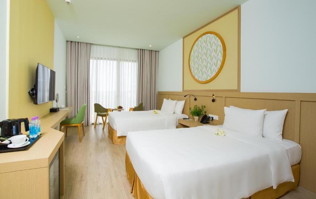Ein Hotelzimmer mit zwei Betten, einem Schreibtisch und einem Fernseher sowie einem großen Fenster mit Vorhängen.
