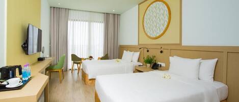 A hotel room with two beds, a desk with a TV, and a large window with curtains.