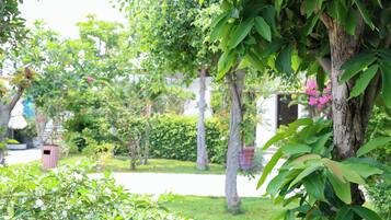 A lush garden with various trees and shrubs, a pathway, and a building in the background.