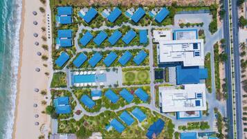 Vista aérea de un resort con varios edificios de techos azules dispuestos en un patrón de cuadrícula, una playa en un lado y una carretera junto a los edificios.