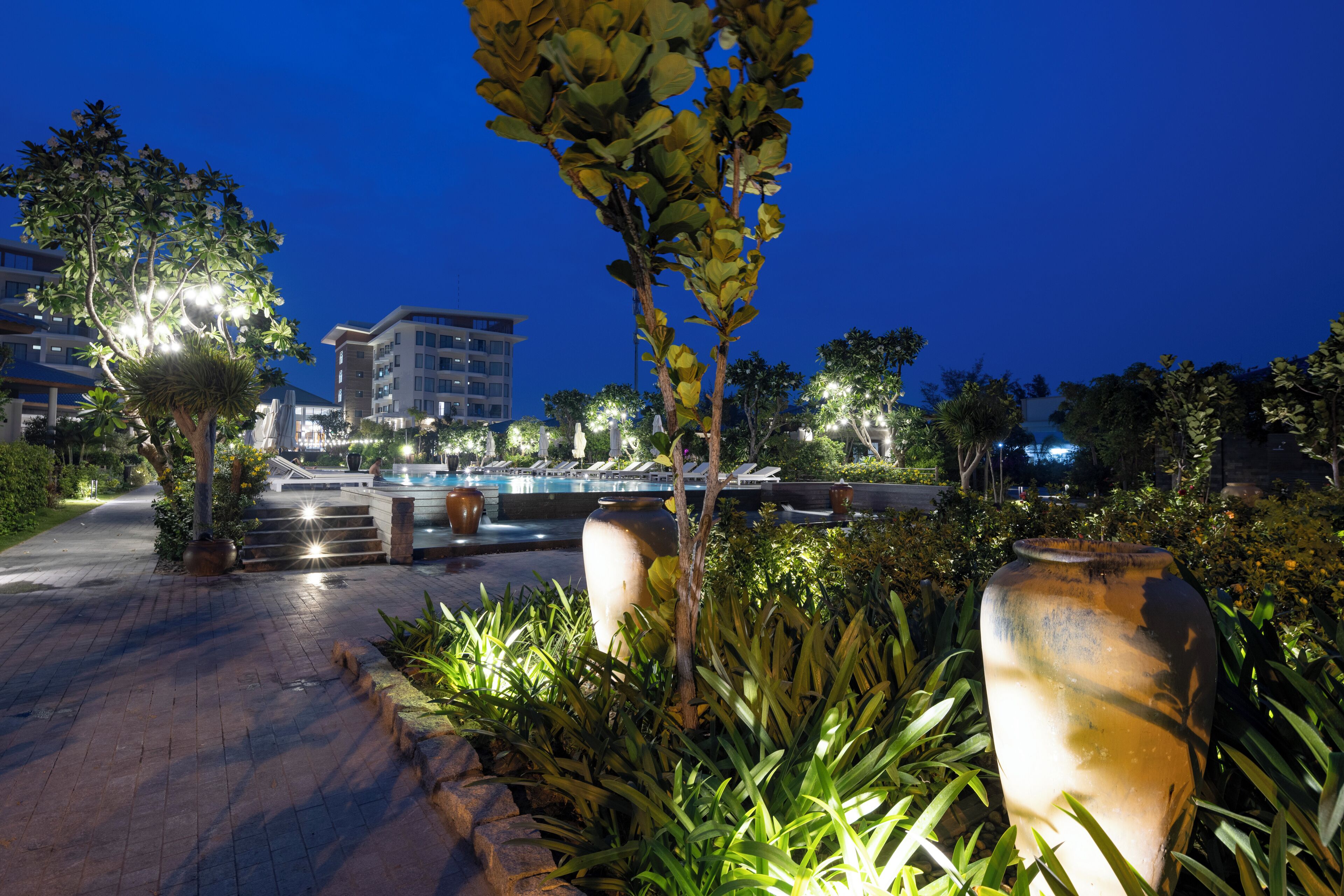 A well-lit outdoor area with a pool, steps leading to a building, and various plants.