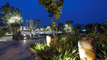 A well-lit outdoor area with a pool, steps leading to a building, and various plants.