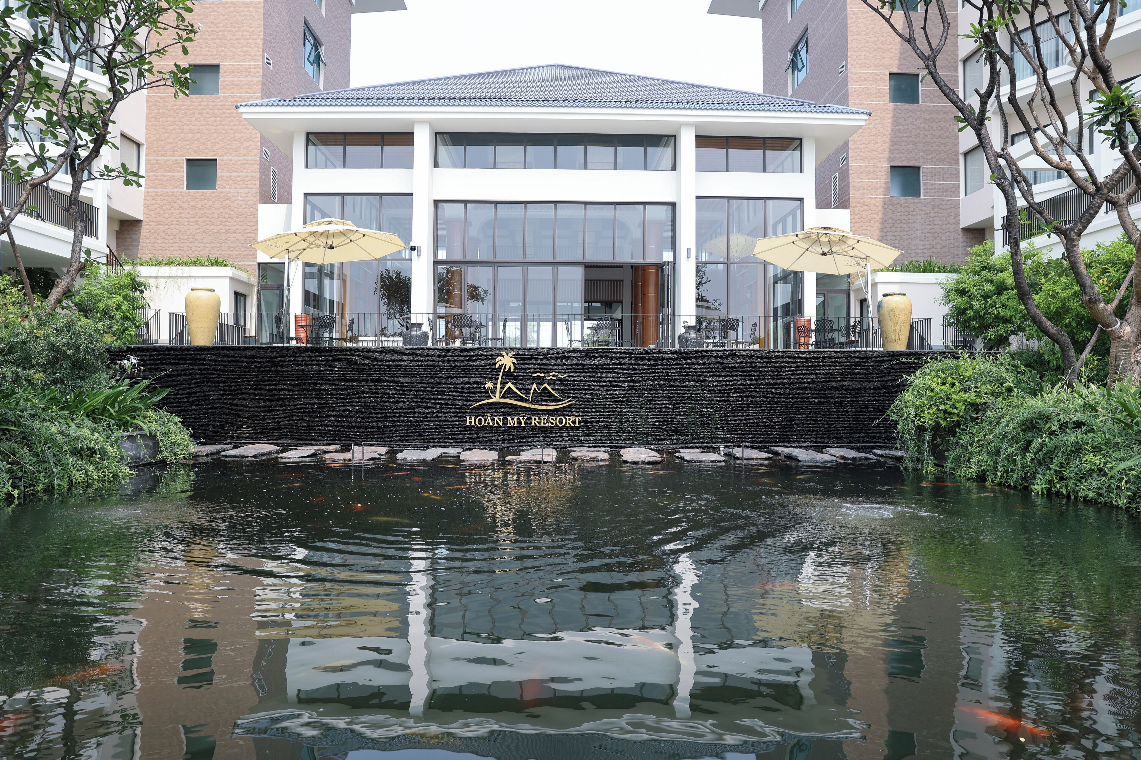 A hotel entrance with a stone wall, outdoor seating, and a koi pond.