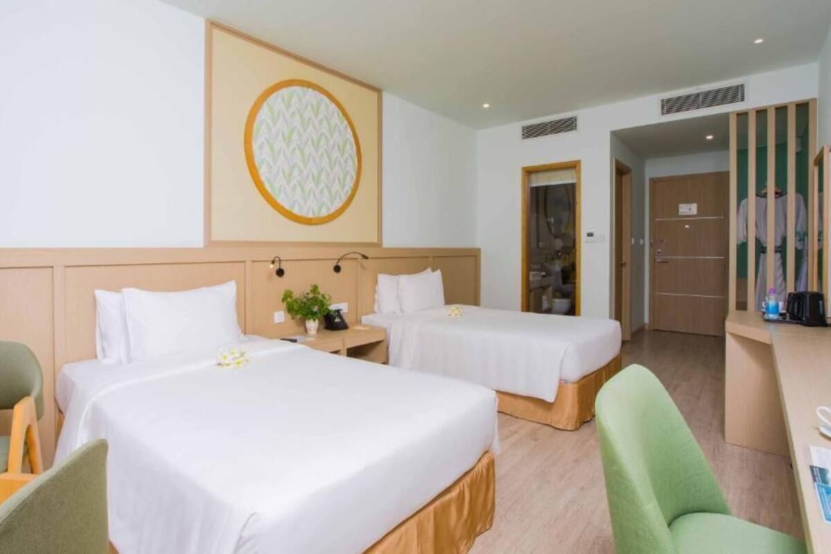 A hotel room with two beds, a desk, a chair, and a wall-mounted TV.
