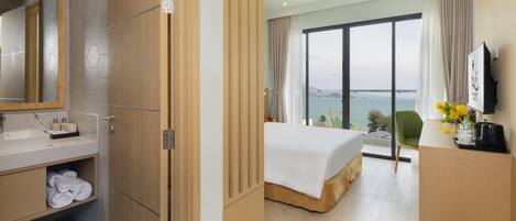 Habitación de hotel con cama, escritorio con cafetera, baño con espejo y lavamanos, y vista al mar.