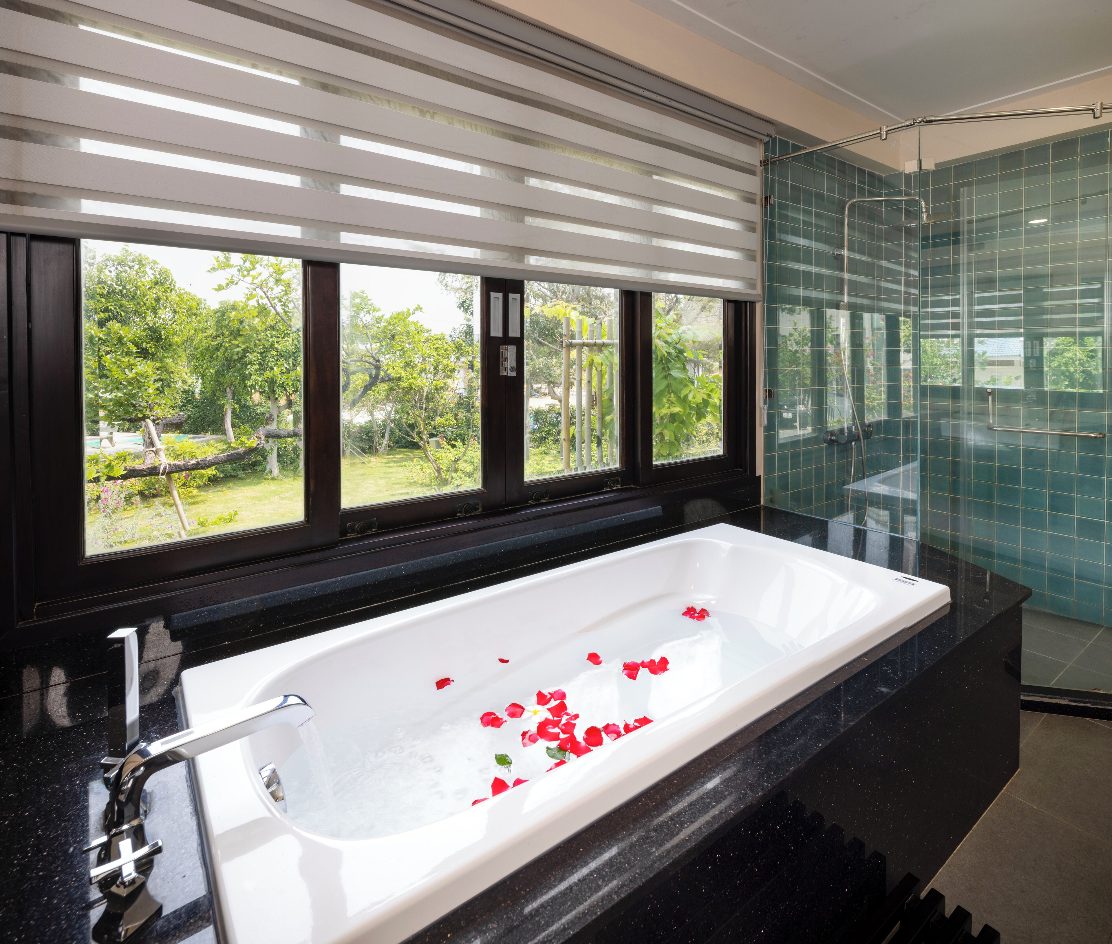 A modern bathroom with a large bathtub, a glass shower enclosure, and a view of greenery through the windows.