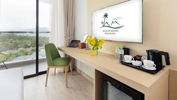 A modern hotel room with a balcony, a desk with a coffee maker, cups, and a vase with flowers.