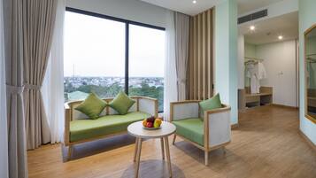 Une chambre d’hôtel moderne dotée d’une grande fenêtre, d’un canapé, d’un fauteuil, d’une petite table avec des fruits et d’un dressing.