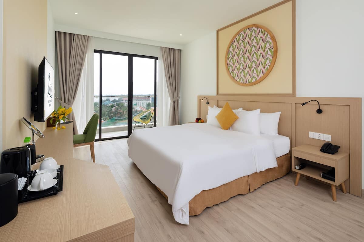 A hotel room with a large bed, a desk with coffee maker and cups, a TV, and a view of the city.