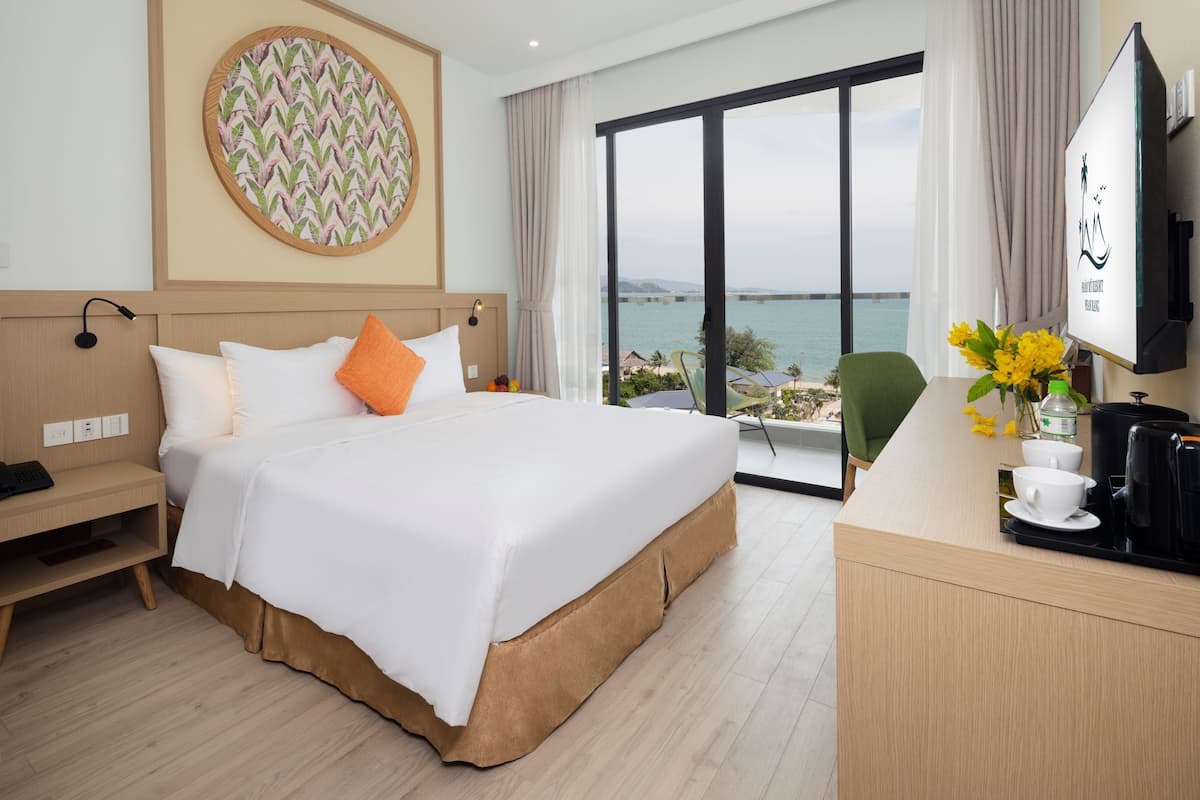 A hotel room with a large bed, a desk with a coffee maker, and a view of the sea.