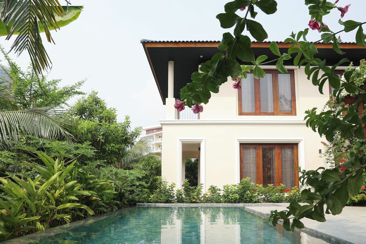 A poolside view of a house with a large window, surrounded by lush greenery.
