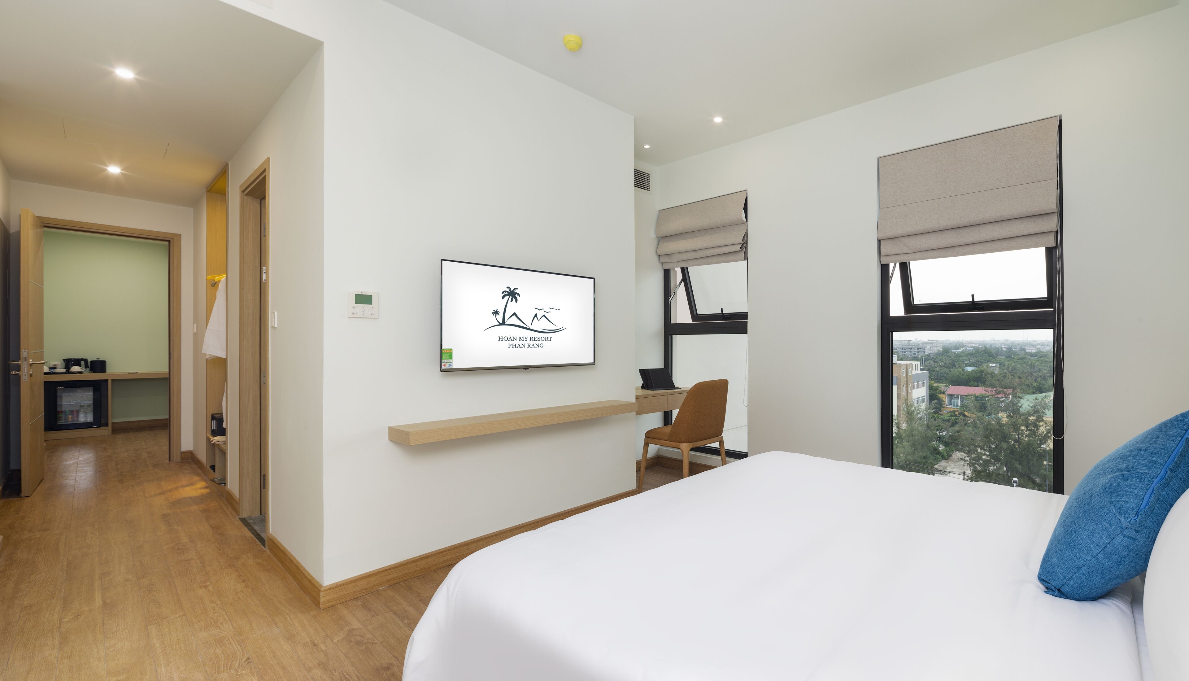 A hotel room with a bed, a desk, a chair, a TV, and a window with a city view.