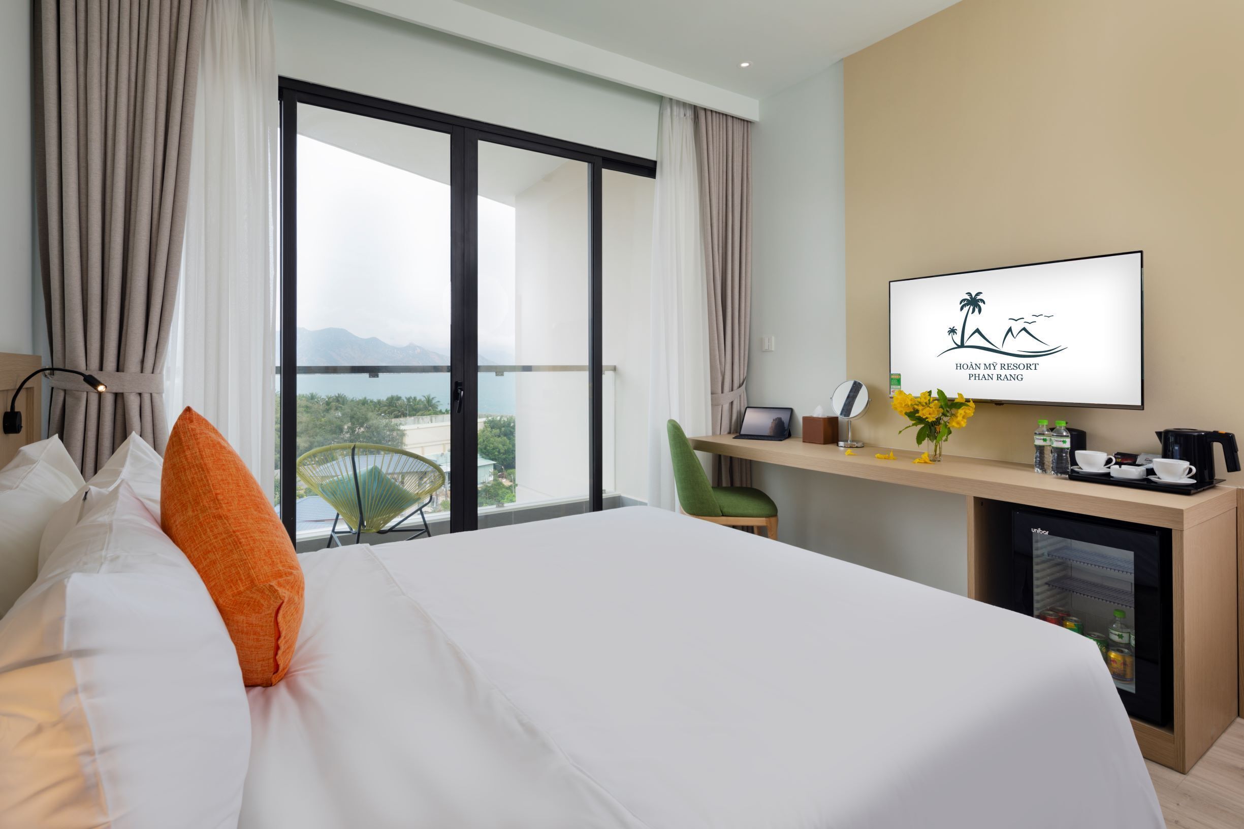 A hotel room with a bed, a desk with a computer, a coffee maker, and a TV displaying the resort's logo.
