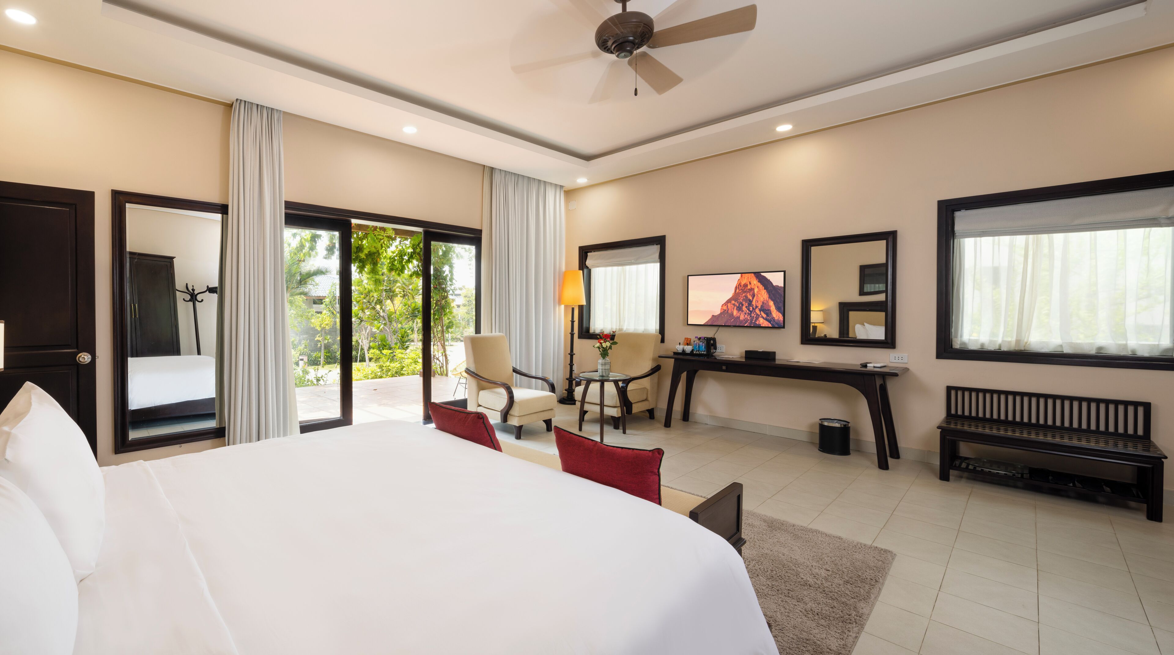 Habitación de hotel con una cama grande, un escritorio, una silla, un televisor y un balcón con cortinas.