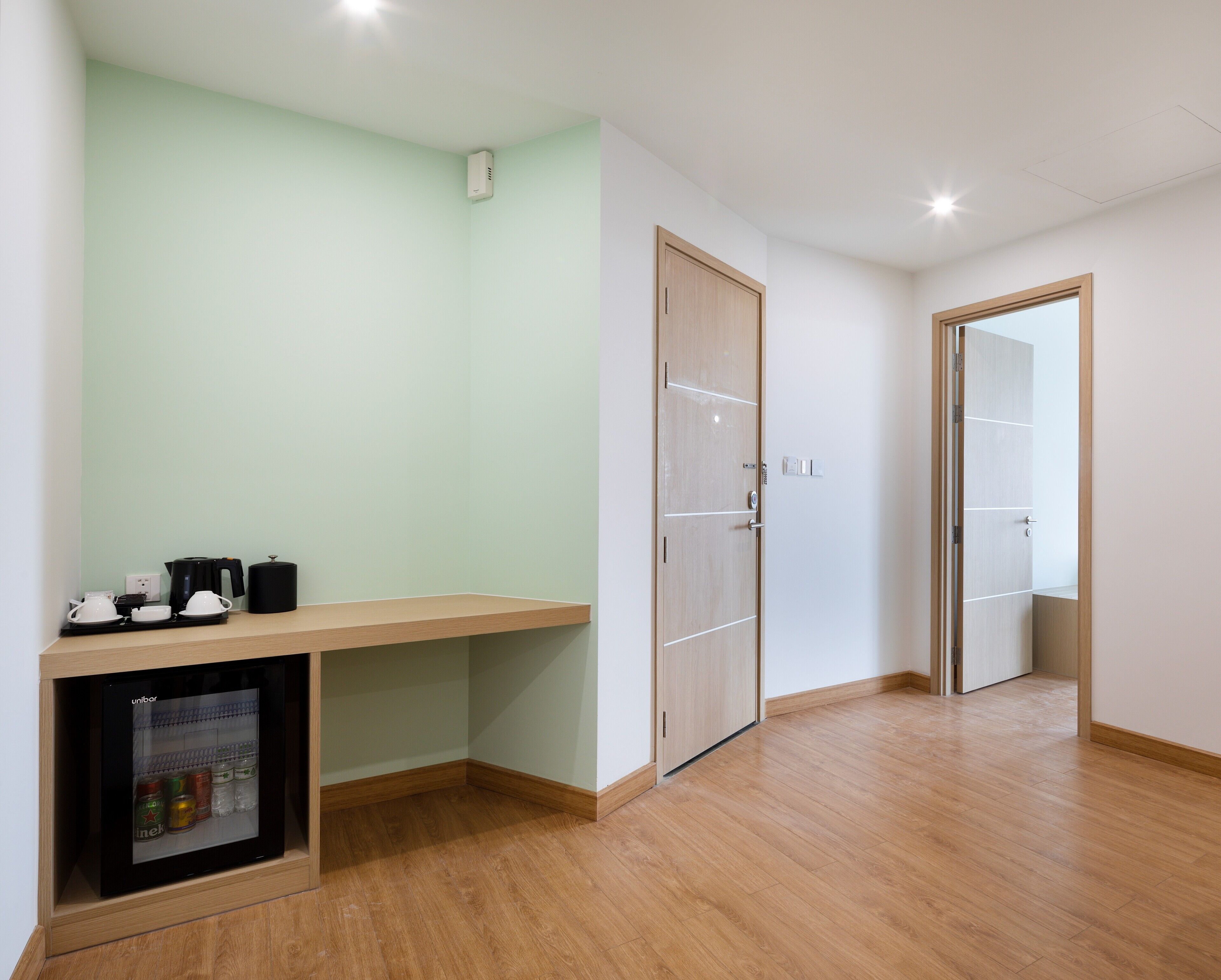 A hotel room with a wooden desk, a minibar, and a door leading to another room.