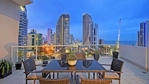 A rooftop terrace with a dining table, chairs, and potted plants. - Savannah Penthouse (Broadbeach)