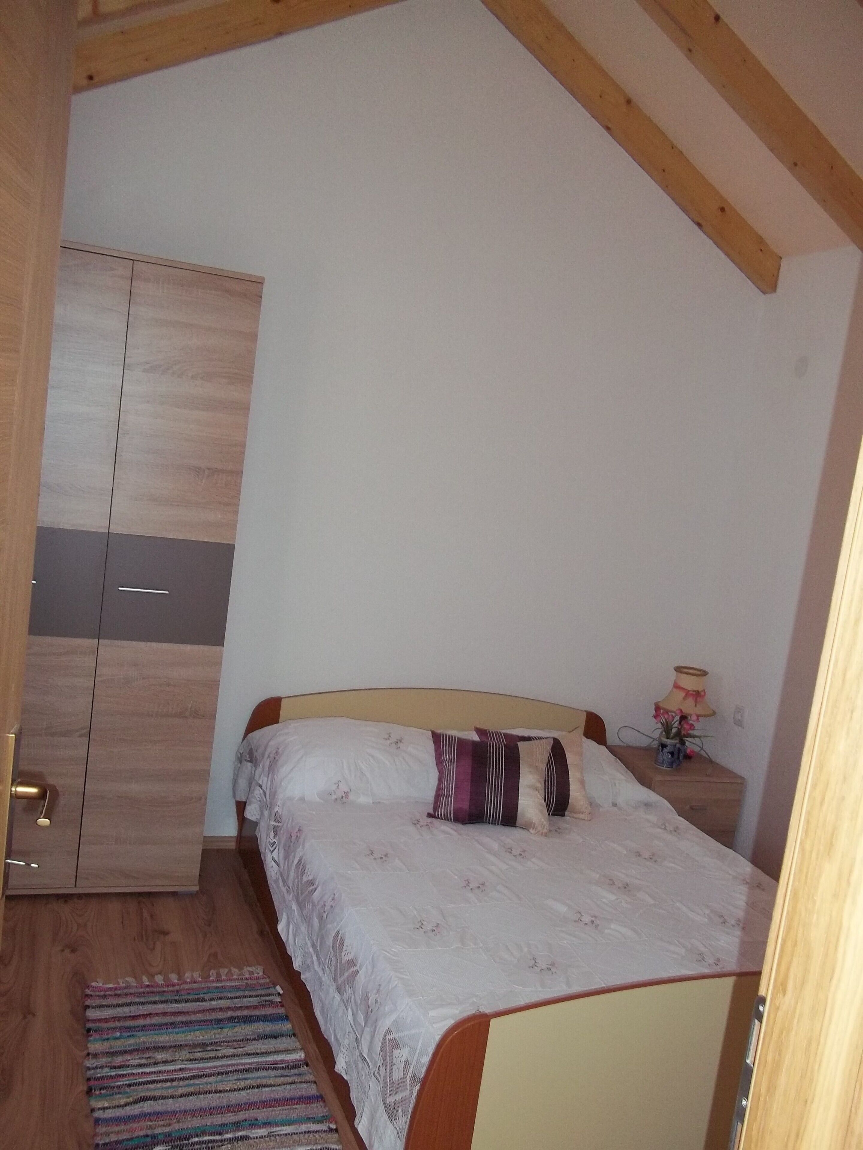 Un dormitorio con una cama, armario de madera y mesita de noche con lámpara.