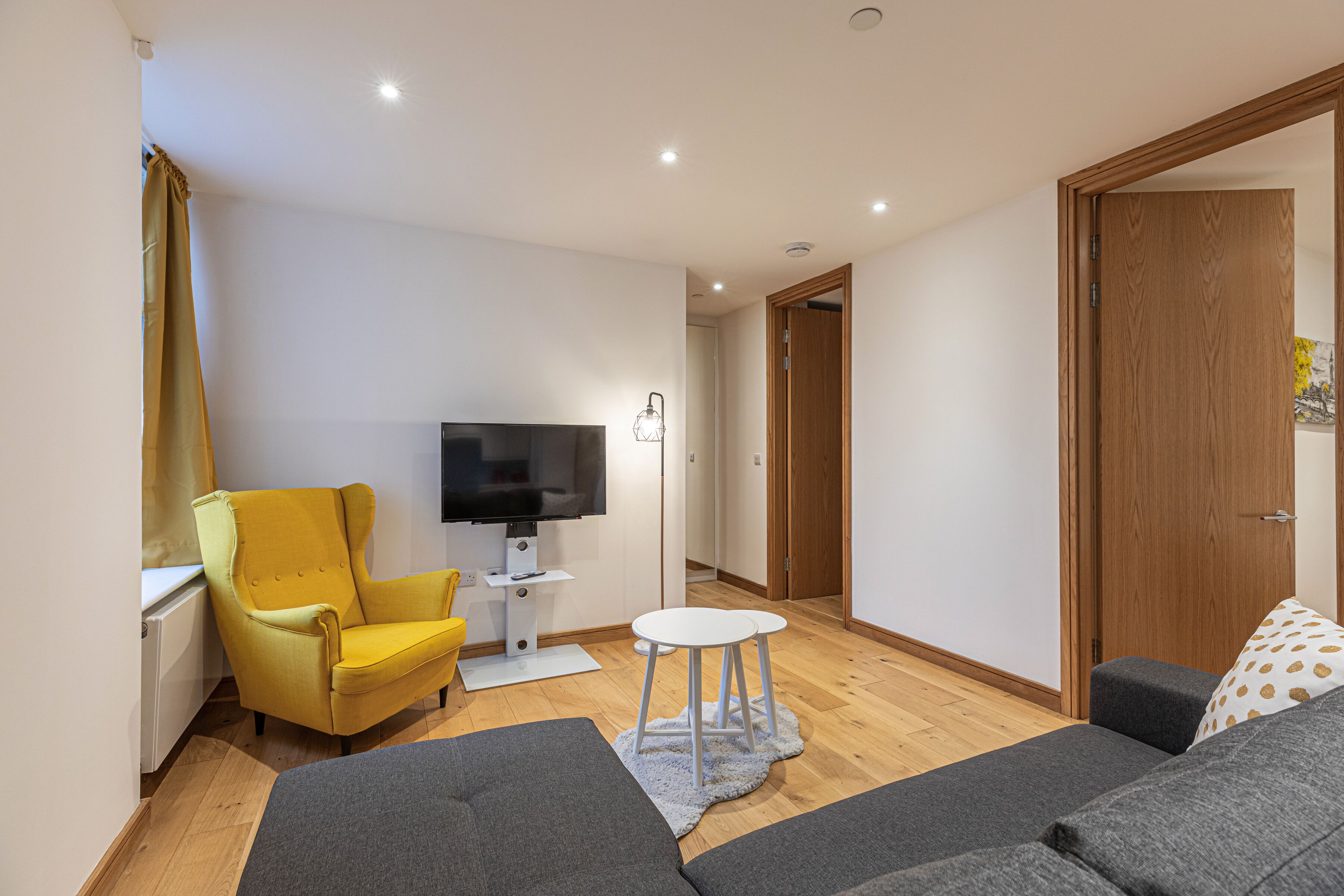 A modern living room with a sofa, a yellow armchair, a TV, and a small white table.