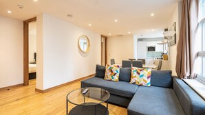 A modern living room with a sofa, a glass coffee table, and a dining area in the background. - Marylebone Apartments (London)