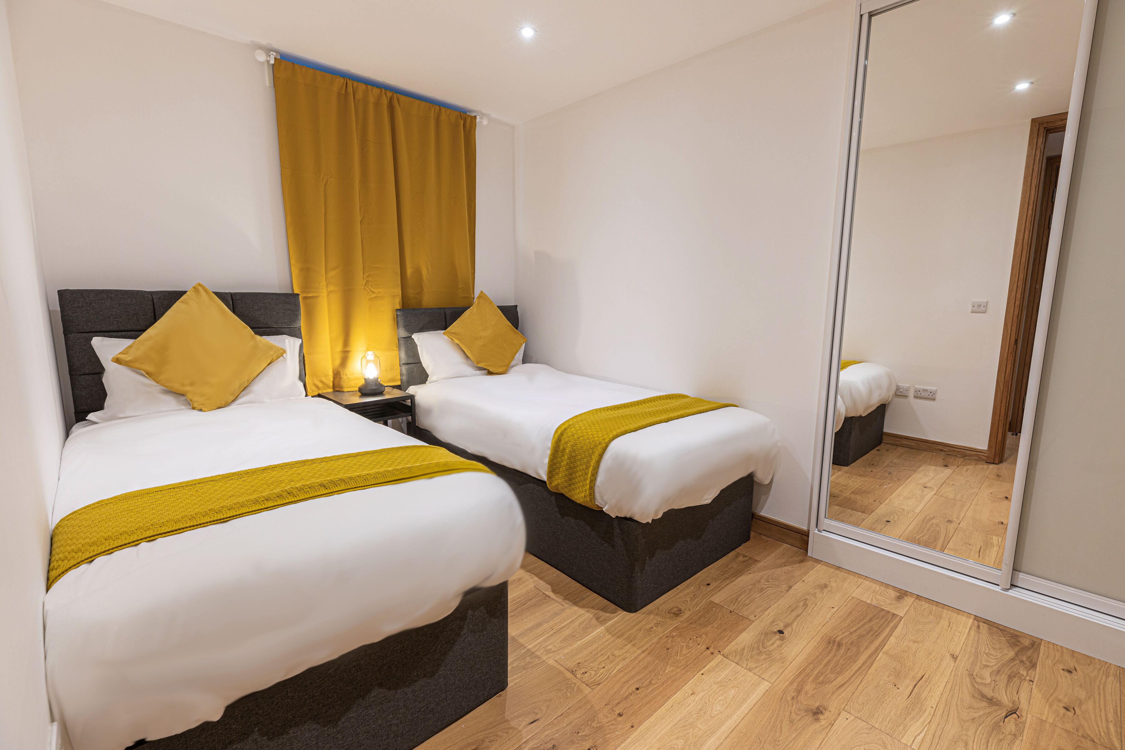 Een hotelkamer met twee bedden, een spiegel en houten vloeren.