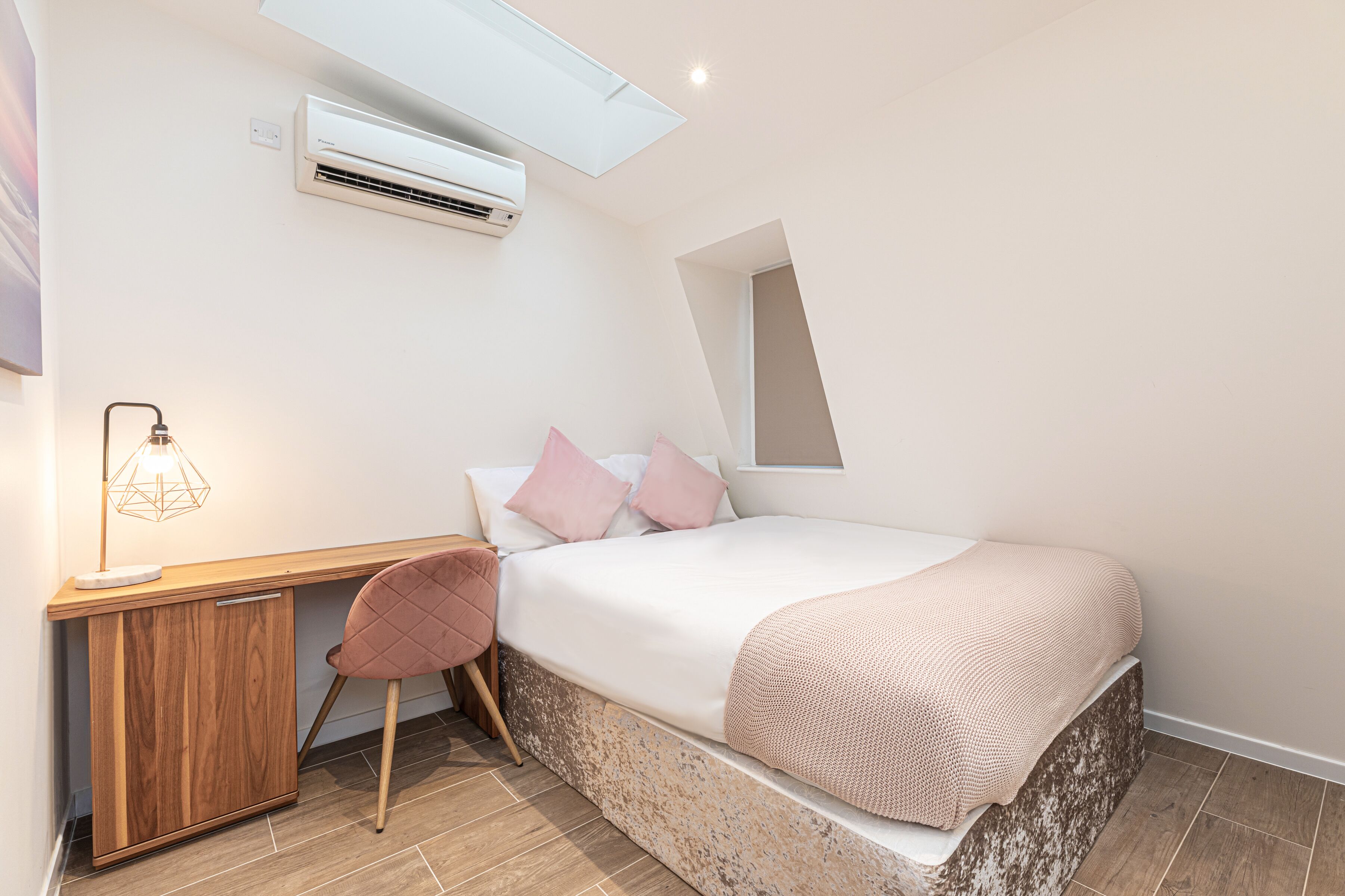Un dormitorio con cama, escritorio, silla, aire acondicionado y ventana.