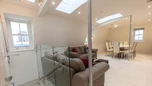 A modern living room with a glass staircase, a sofa set, and a dining area with chairs and a table. - Marylebone Apartments (London)