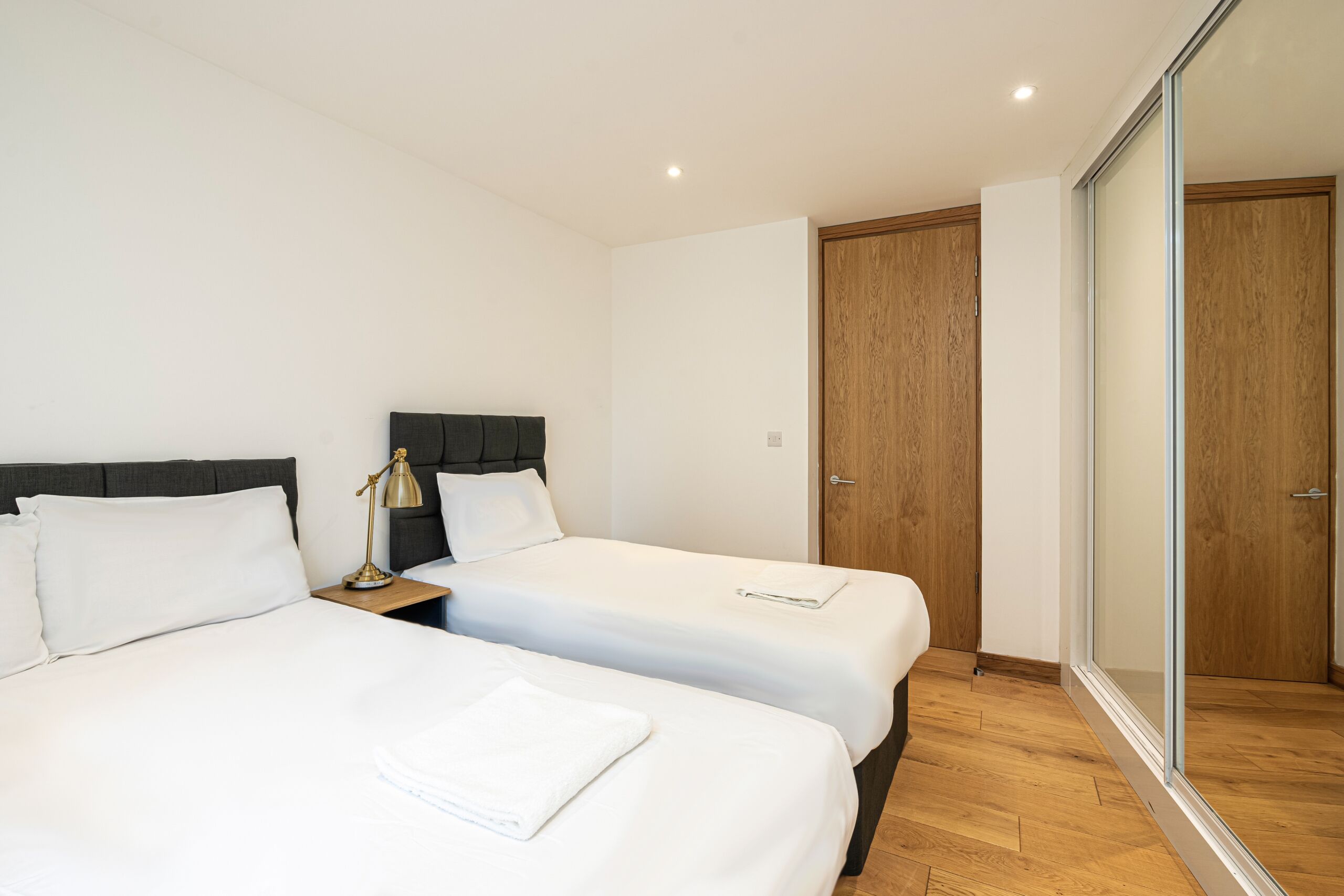 Habitación de hotel con dos camas, una mesita de noche, una lámpara y una puerta corrediza al baño.