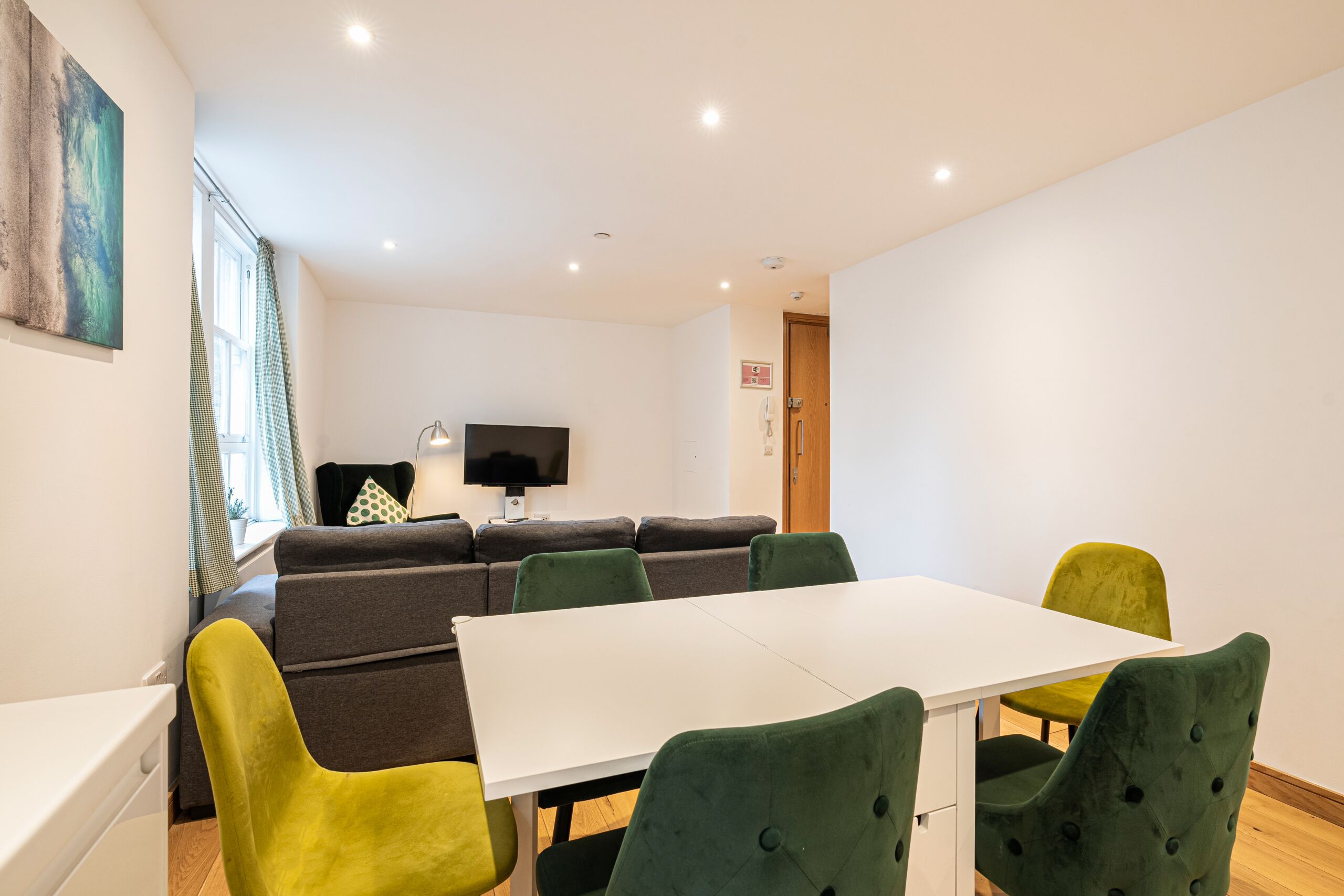 Una sala de estar moderna con una mesa blanca, sillas verdes y amarillas, un sofá gris y un televisor de pantalla plana.