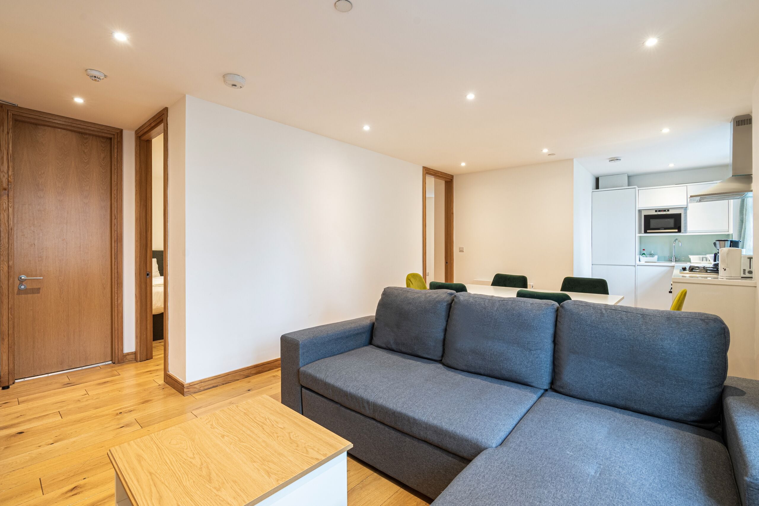 A modern living room with a grey sectional sofa, wooden flooring, and a small wooden coffee table.