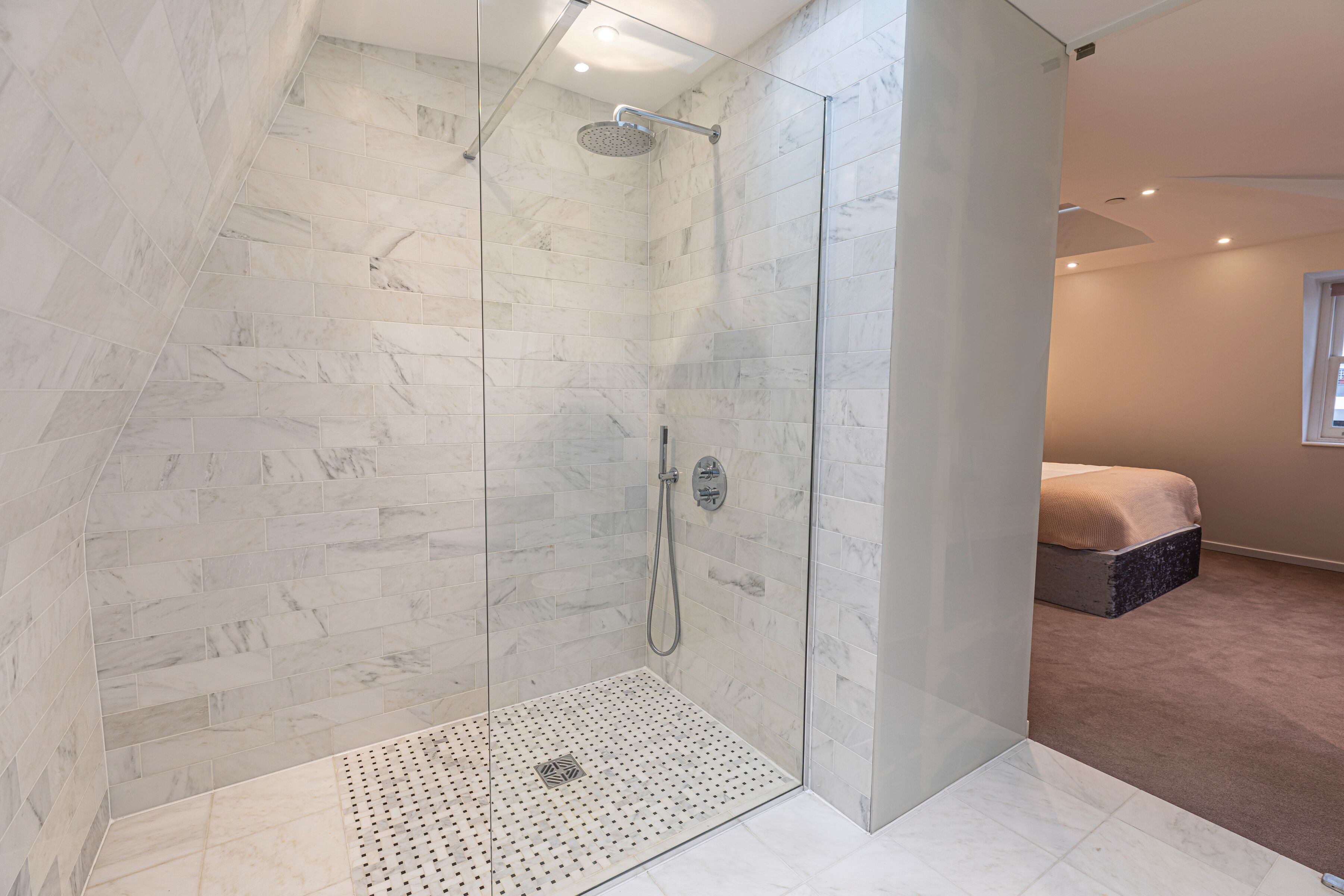 A modern bathroom with a glass-enclosed shower, marble tiles, and a small, perforated shower floor.