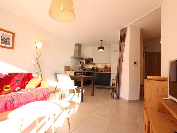 A modern living room with a sofa, chairs, a TV, and a kitchen in the background. - Cosy 2-Room Apartment in Briançon, Terrace, 4 Guests, WiFi, Parking, 3-Star Rating (Briançon)