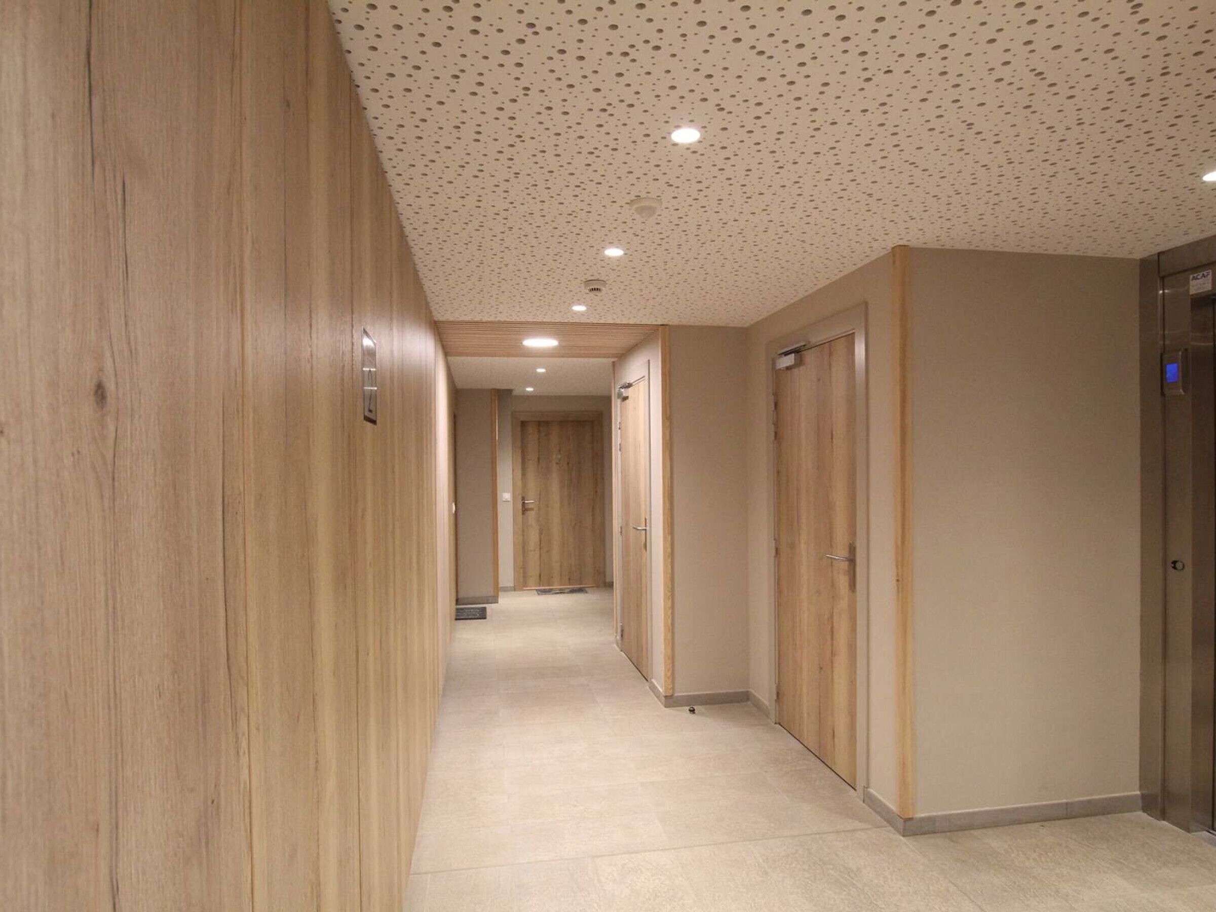 A hallway with wooden walls and doors, a tiled floor, and a ceiling with recessed lighting.